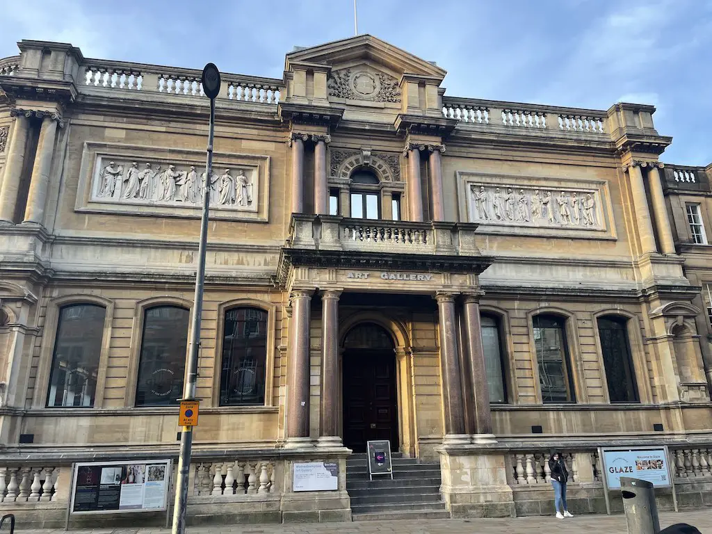 The Wolverhampton Art Gallery, a majestic, neoclassical building with a towering facade adorned with intricate stone carvings. The gallery features a grand entrance framed by elegant columns and a balcony overlooking the street. The inscription "ART GALLERY" proudly proclaims the building's purpose, inviting visitors to explore the cultural treasures within.