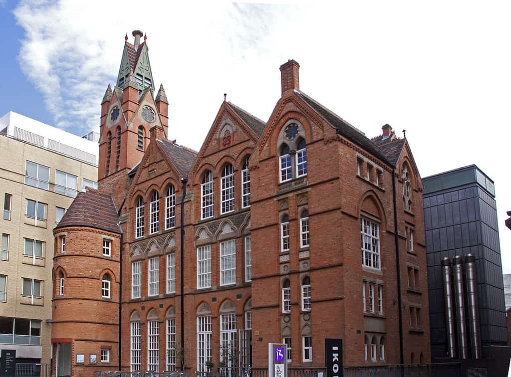 an old victorian red brick building housing a gallery, with cylindrical spiral tower in front and clocktower at back, and numerous, white-framed windows