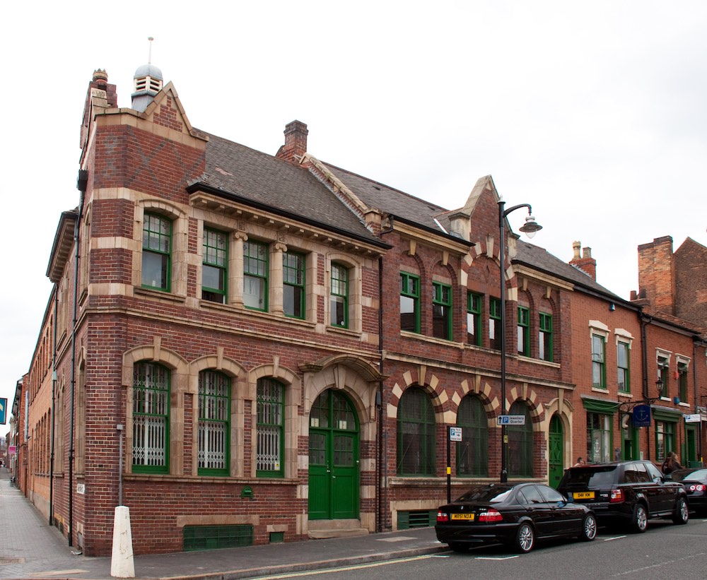 view of the front and the side of the museum of the jewellery quarter building with its red bricks and green doors and window frames, in birmingham, england.