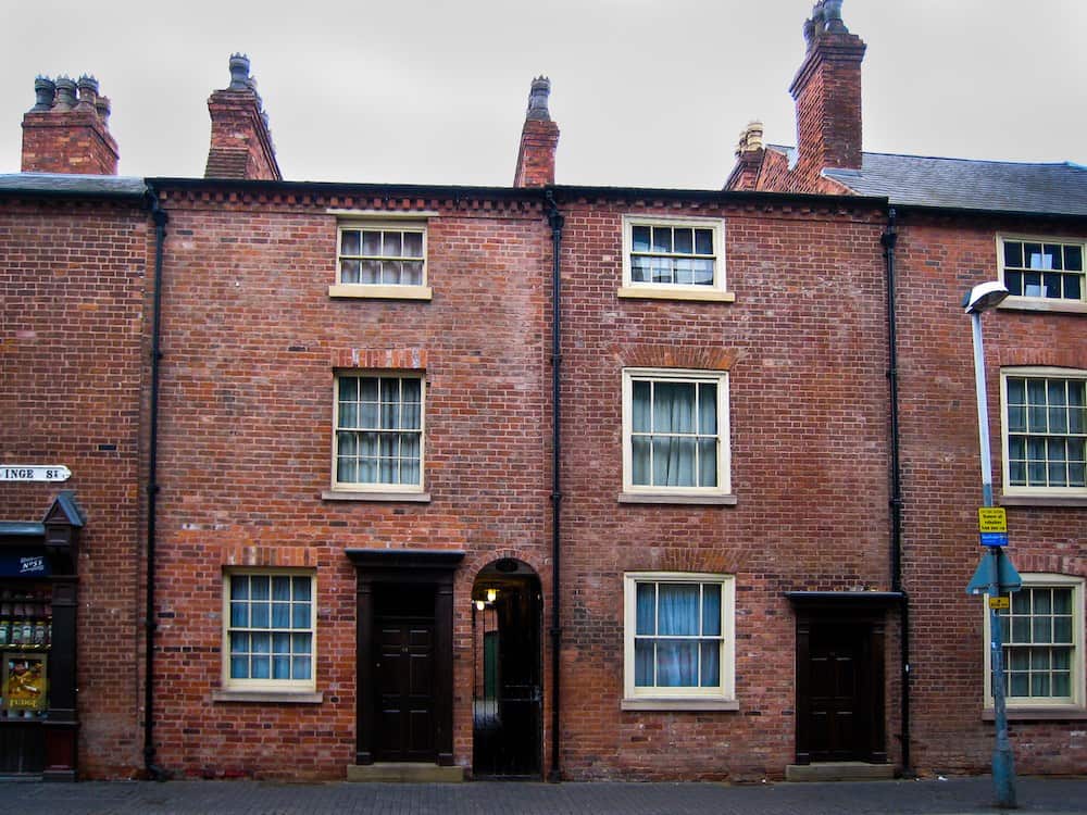 a line of victorian-era, terraced brick houses with cream-framed windows and dark brown doors, with a cloudy, rainy sky.