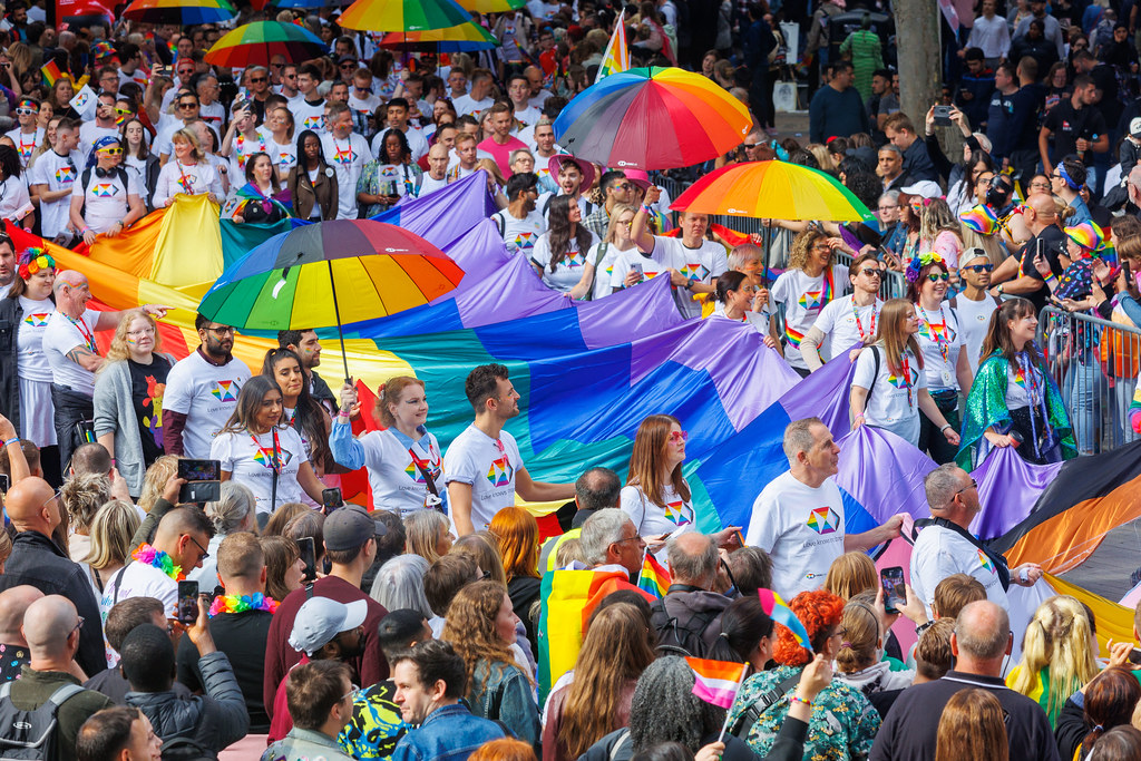 close up of festival-goers clad in bright colours holding a long rainbow banner, marching though the city centre for birmingham pride festival