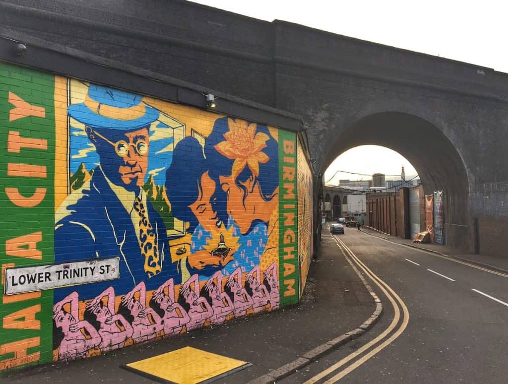 brightly coloured mural on a street corner leading to a derelict street going under an old railway bridge in the digbeth region of birmingham, england