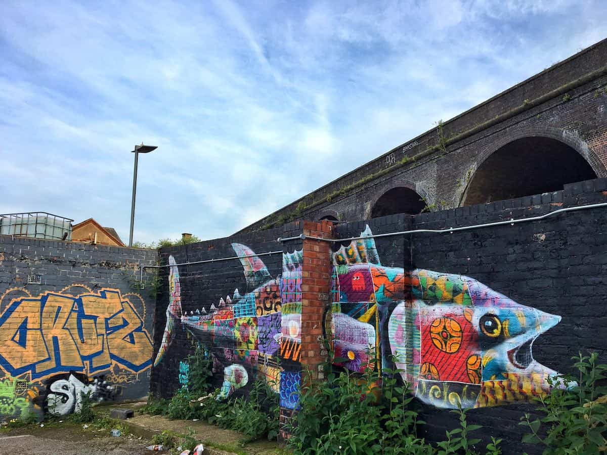 bright-coloured graffiti art of a fish on dark brick walls with a railway bridge in the background