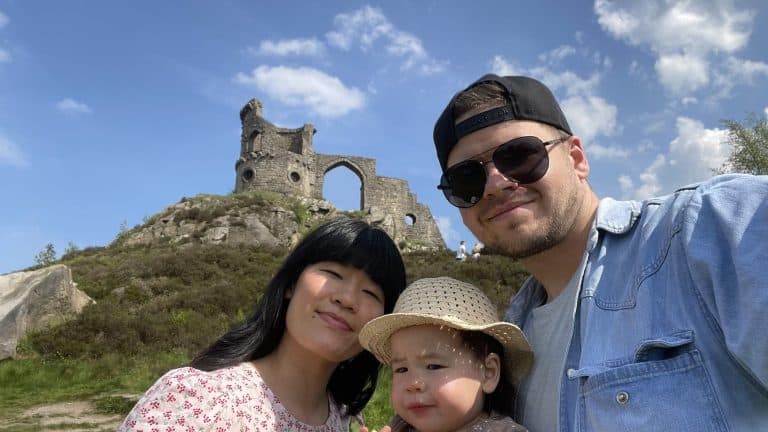 a young couple with their toddler daughter posing in front of a castle ruin atop a hill at mow cop, staffordshire.
