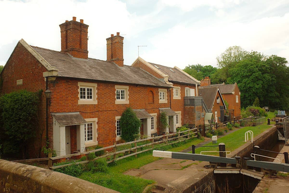 a line of four or five old english country houses with a canal lock in front, surrounded by countryside trees