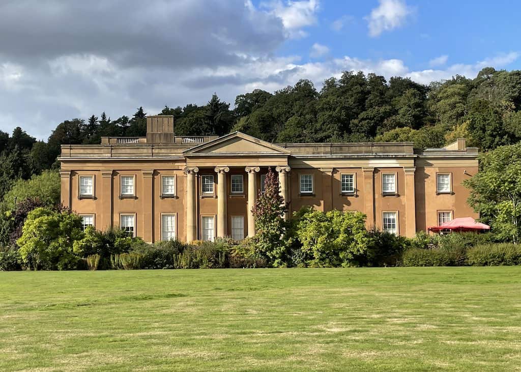 Himley Hall park, a grand Georgian mansion surrounded by lush green parkland. The building features a central portico with columns and a symmetrical facade.