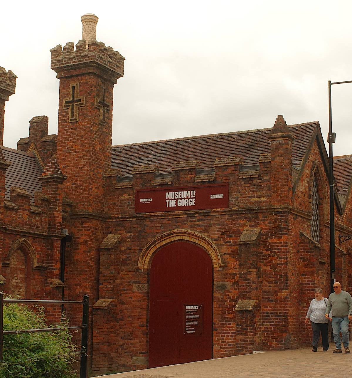 A historic red brick building with a castle-like appearance, featuring arched windows and turrets, identified as the "Museum of the Gorge."