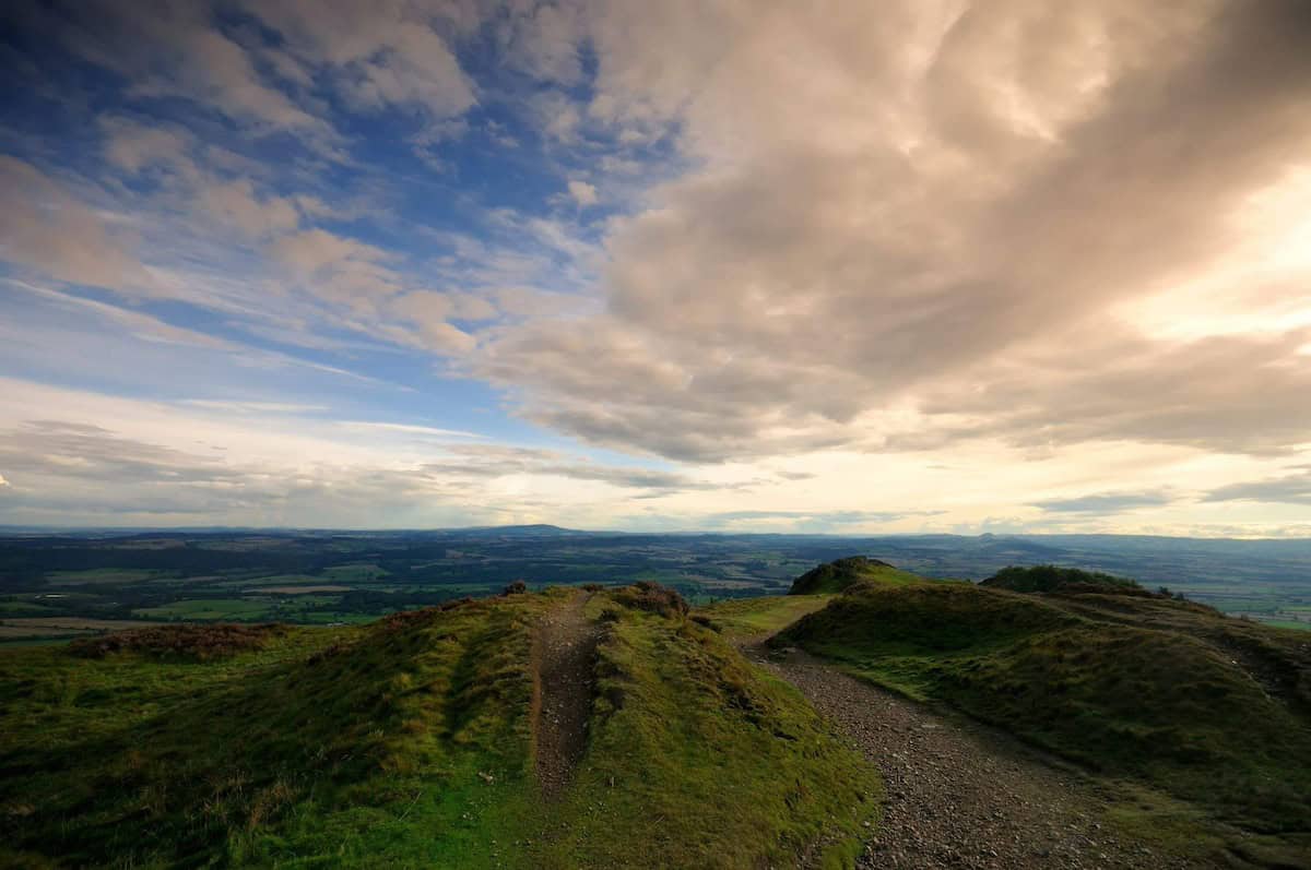 large clouds looming over the small hills at the peak of the wrekin, with vast countryside visible in the distance