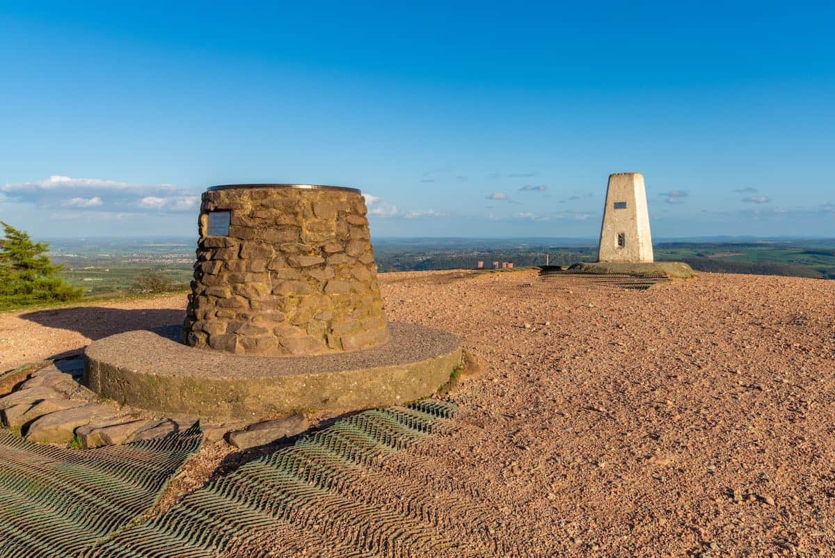 view from the peak of the wrekin hill with an iron age hill fort at the forefront and a monument at the back, and aerial views of the vast countryside in the background