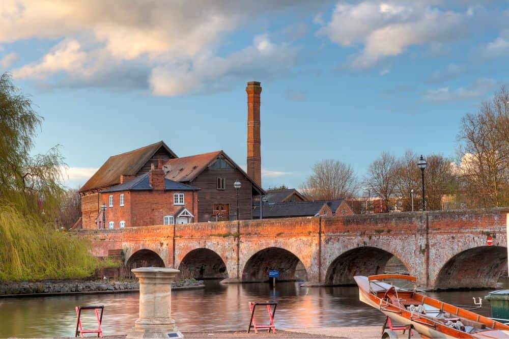 Stratford-upon-Avon and a river with a medieval bridge over it, with some buildings and a tall chimney behind it