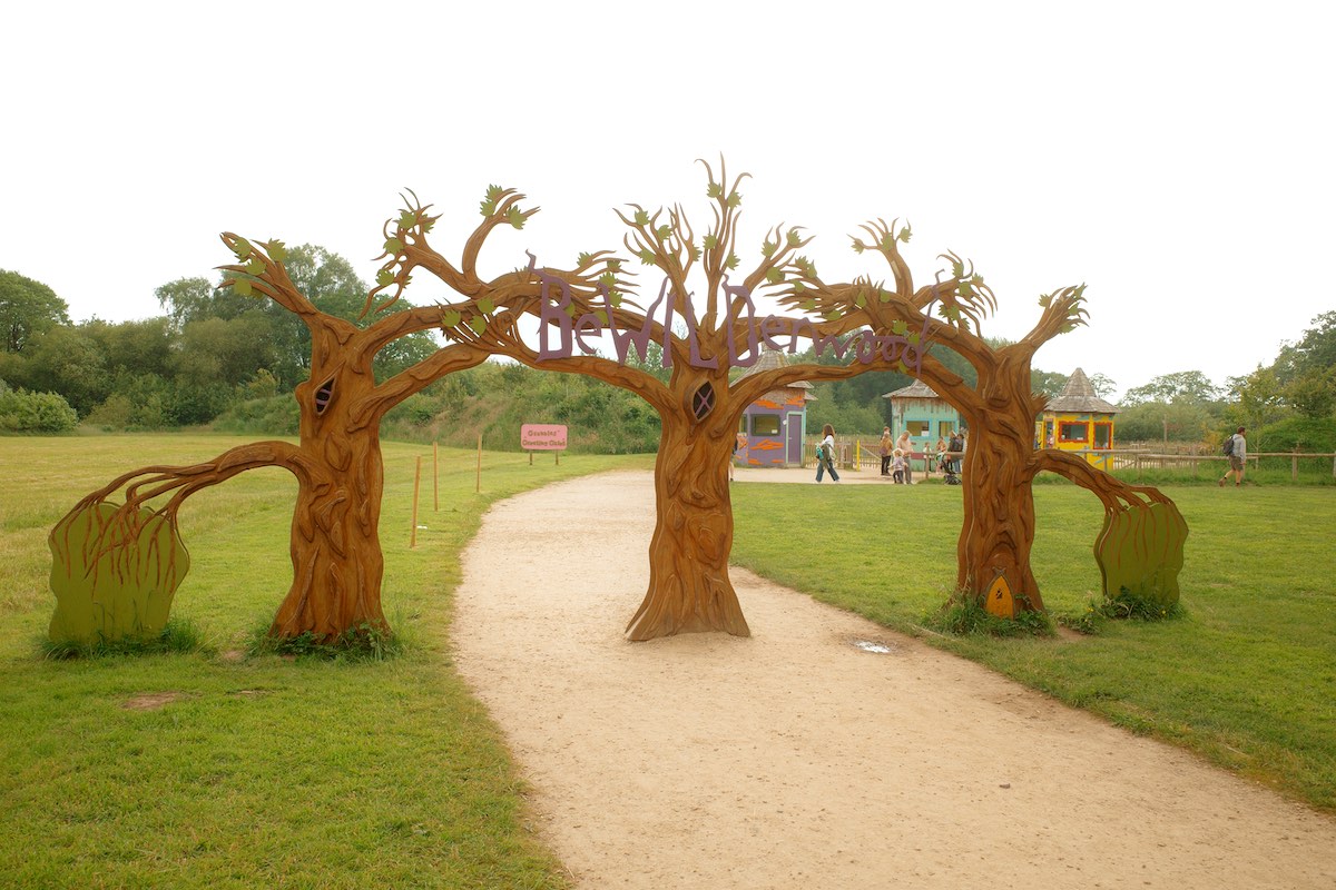 large entrance frame shaped like three trees with wonky branches and a path leading through to some brightly coloured huts