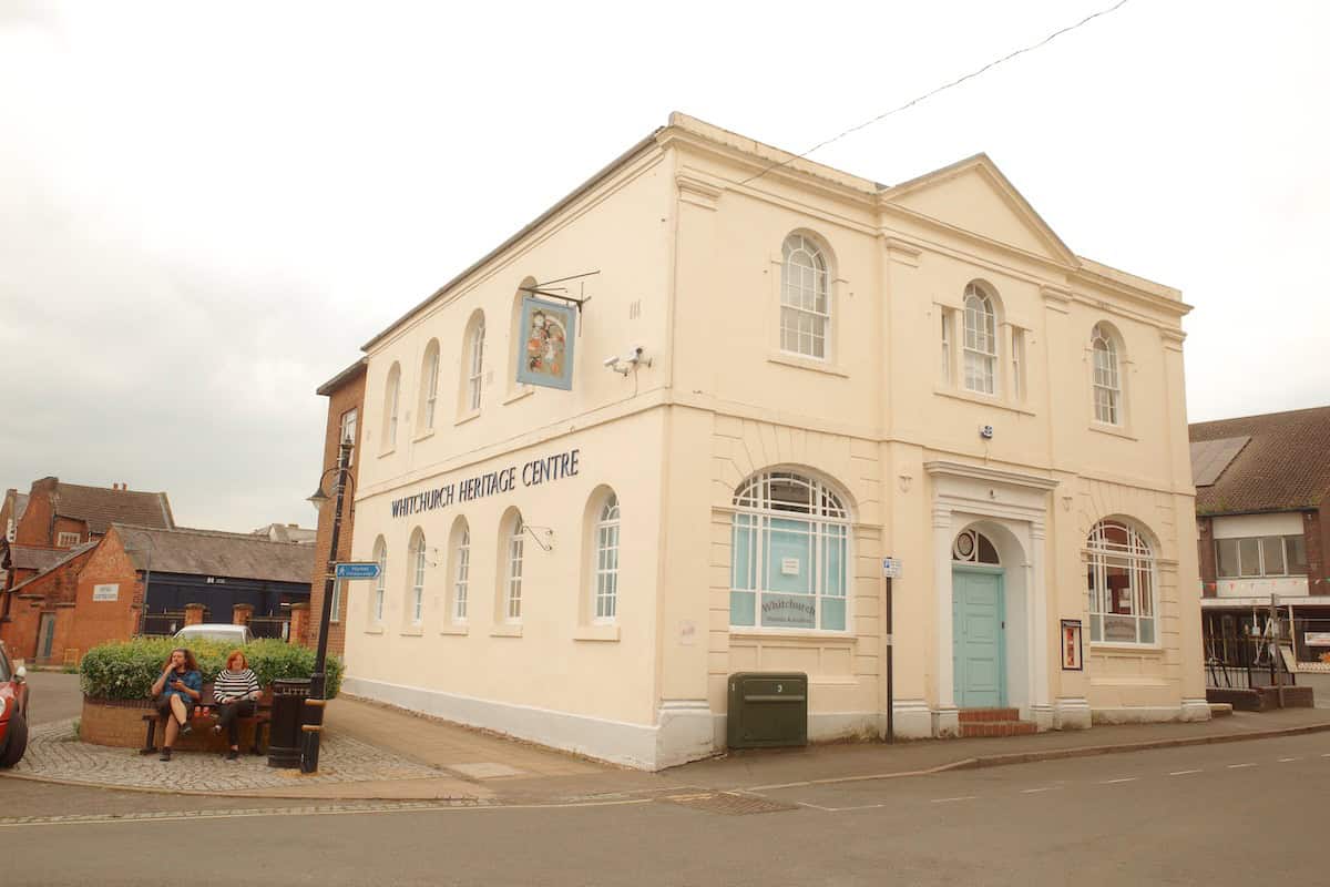 large white early 20th century building with pastel blue door and arched white framed windows