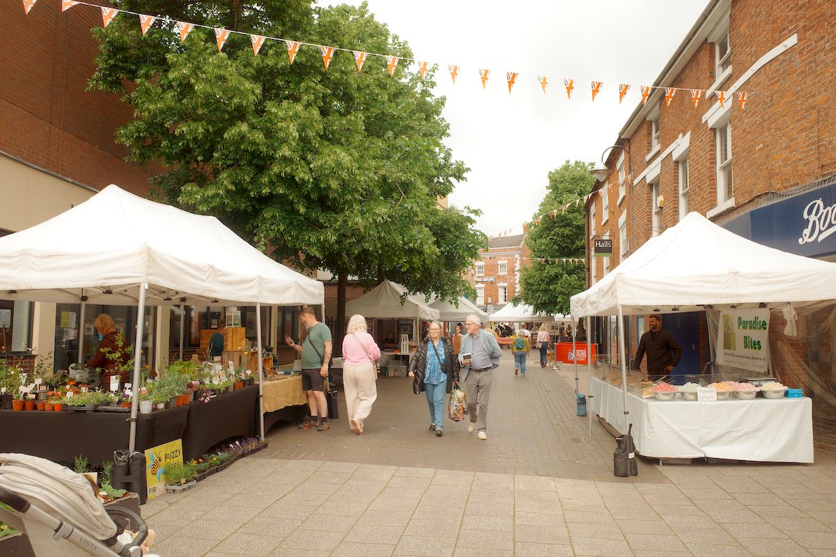 white marquee tents in a market place with produce on sale and people browsing