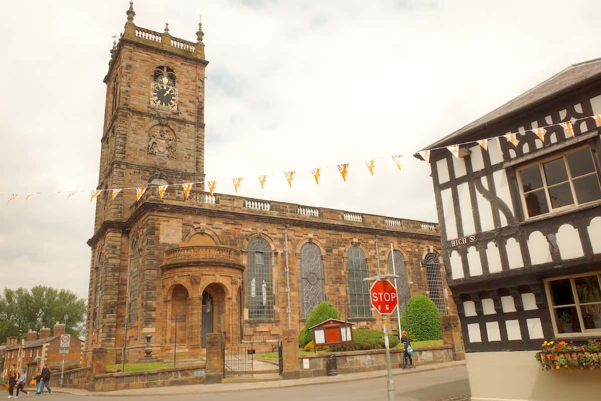 large medieval church with clock tower on edge of town centre with tudor building in forefront right side