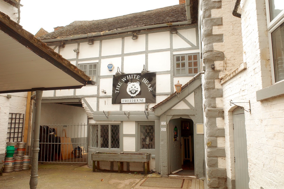 a white timber-framed tudor building within a courtyard off the high street with large black sign saying the white bear
