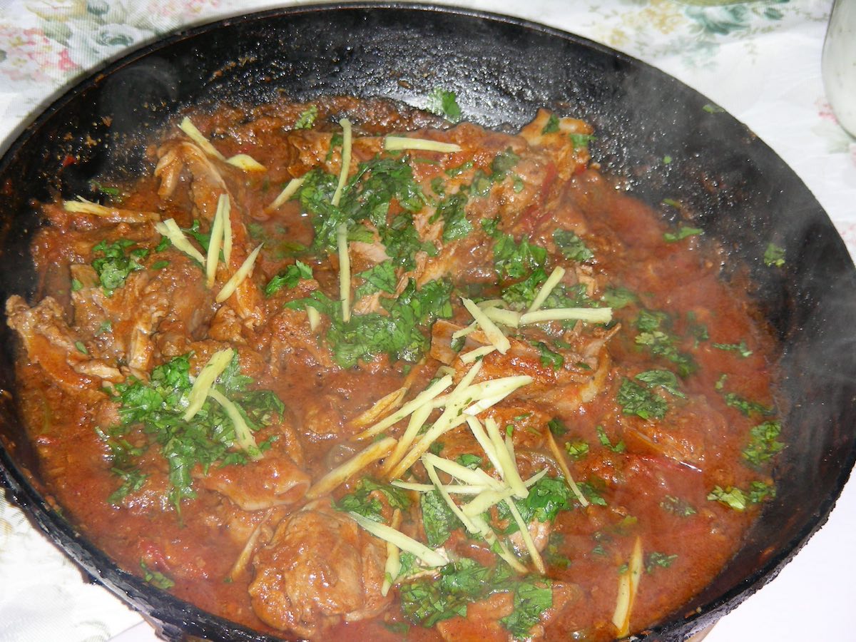 close up of an iron serving bowl with a curry dish known as balti, comprising of tomatoes, coriander, meat, ginger and other spices and herbs, steaming hot 