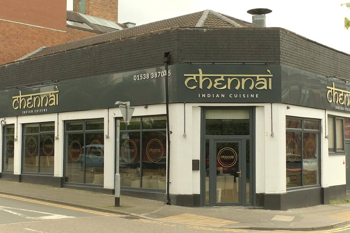 a black and white decorated restaurant on a street corner, with golden name sign in Indian style lettering and large, dark glass windows.