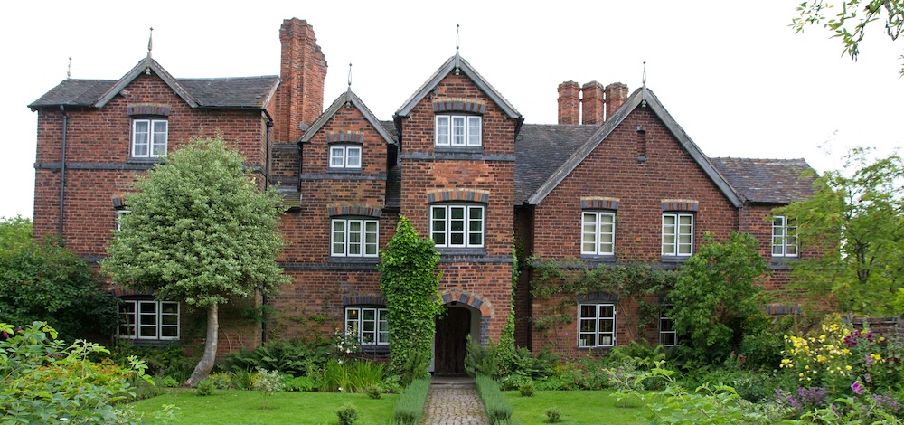 large stately country manor house surrounded by trees and neatly trimmed lawn