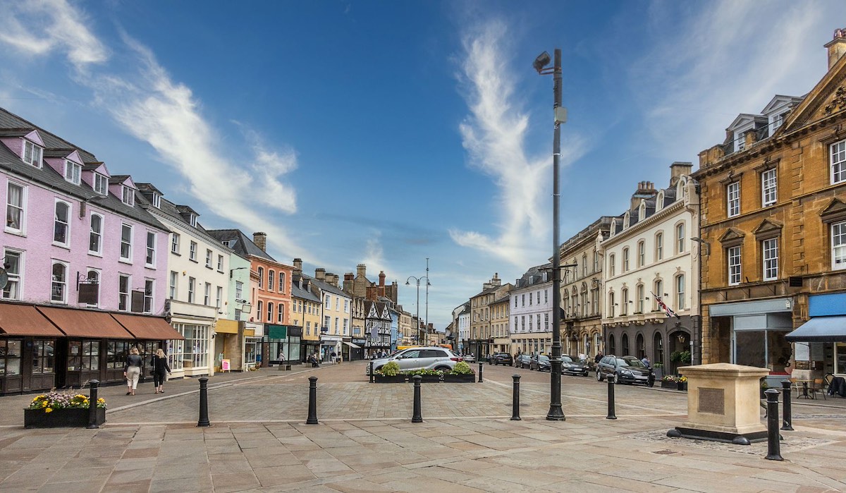 A wide high street in a Cotswold town with colorful buildings and shops lining both sides.