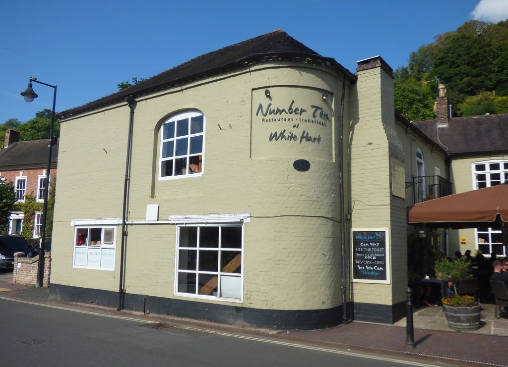 A cream-colored building with "Number Ten Restaurant-Tearooms at White Hart" painted on its curved exterior wall. The building has white-framed windows, a black roof, and appears to be in a small town setting with greenery visible in the background.