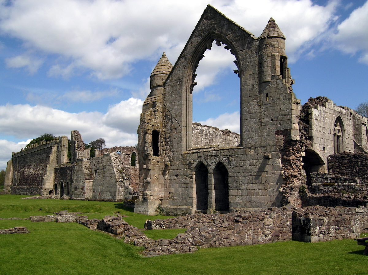 a large site of medieval stone ruins of a chapter house with large arched hollow windows and doorways