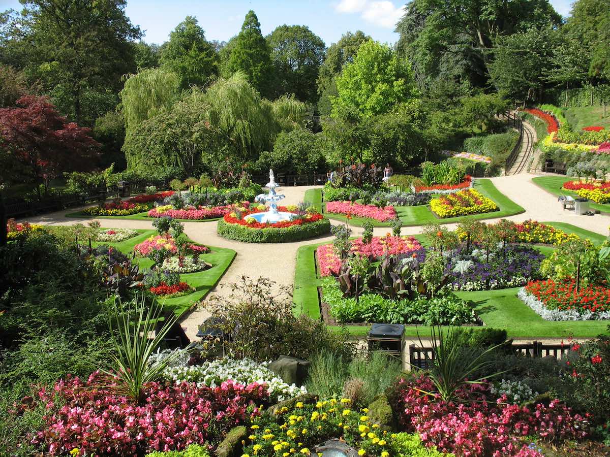 stunning gardens with brightly coloured flowers, neatly trimmed lawns, pathways and trees in the background