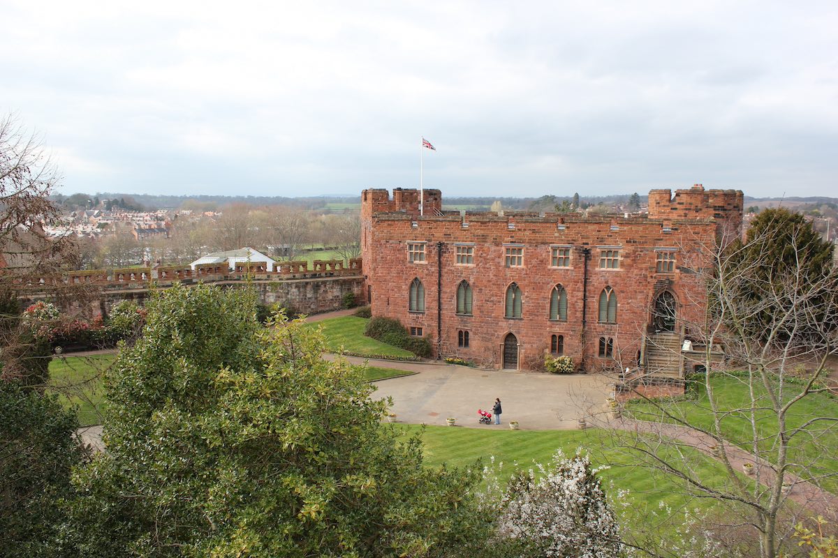 large red sandstone castle with arched windows and castle walls covering vast area of grassy hills