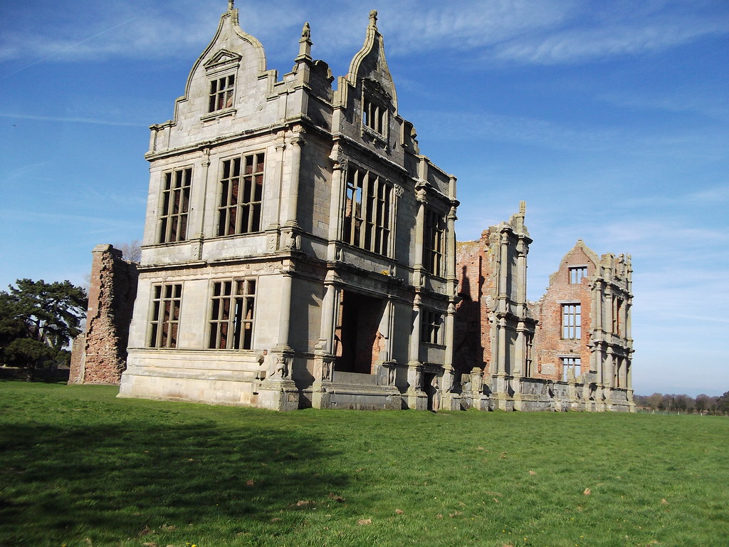 an old medieval and 17th-century castle ruin with arched frames on a green lawn amidst a clear blue sky backdrop