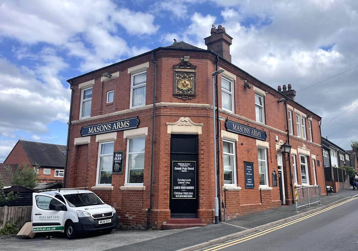The Masons Arms, a Victorian-era red brick corner pub with ornate architectural details, featuring large windows, decorative stonework, and traditional pub signage. A white van is parked outside on the street.