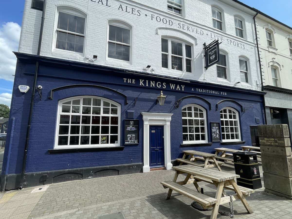 The Kings Way, a traditional pub with a striking blue-painted lower level and white upper floors, featuring large arched windows and outdoor wooden picnic tables, described as "A Traditional Pub" on its signage.