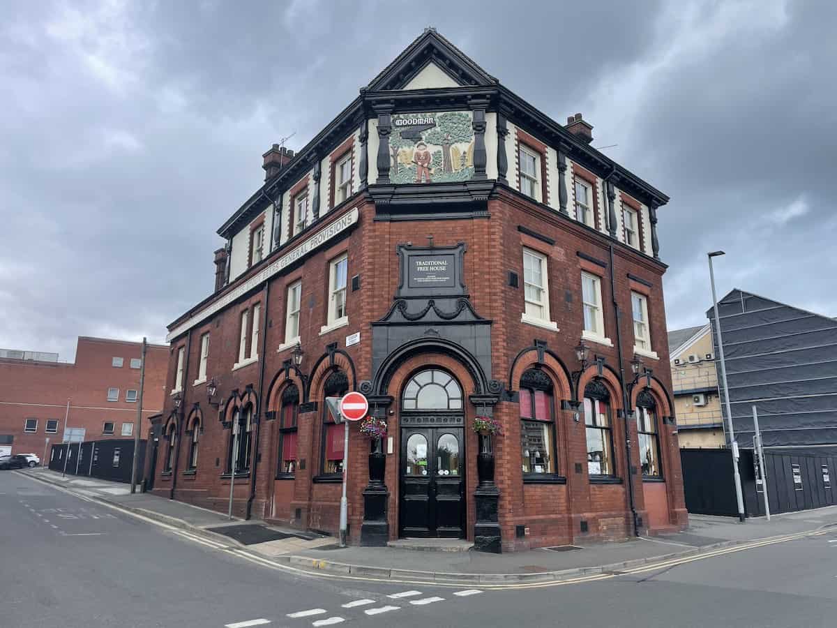 A grand Victorian corner pub building with red brick construction and ornate black-painted architectural details, with a sign name displaying "the Woodman", and featuring arched windows and decorative stonework.