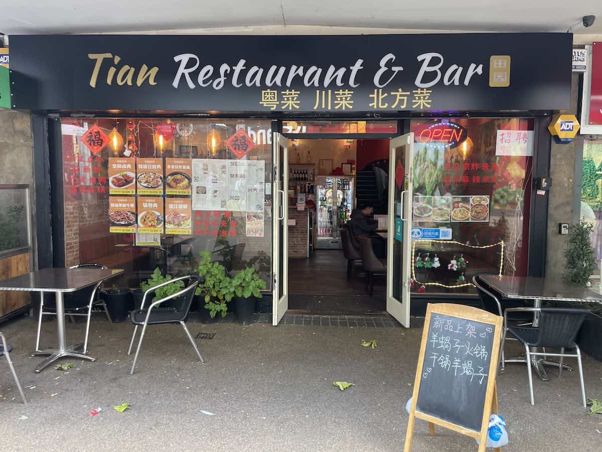Tian Restaurant & Bar, a Chinese restaurant with bilingual signage in English and Chinese characters. The storefront has a dark facade with red lanterns hanging outside, menu displays in the windows, and outdoor seating with metal chairs and tables.