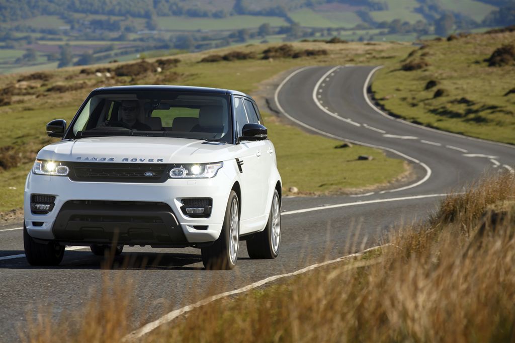 A white range rover driving towards the camera on a winding countryside road