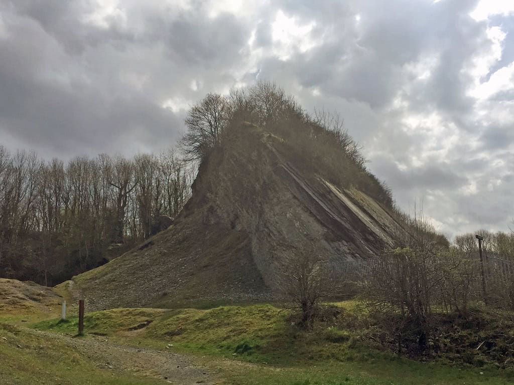 a tall, triangular rocky hill called Wren's Nest, with trees at the top and a steep, almost smooth cliff face on one side.