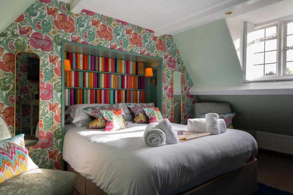 A bright and colourful double bedroom in The Dial House hotel, with vibrant floral prints on one wall and a stylish mix of patterned textiles and cushions on the white bed with white rolled towels.