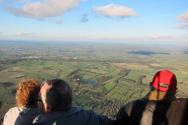 birds eye view of the countryside from inside a hot air balloon, with three people admiring the views from the hot air balloon.