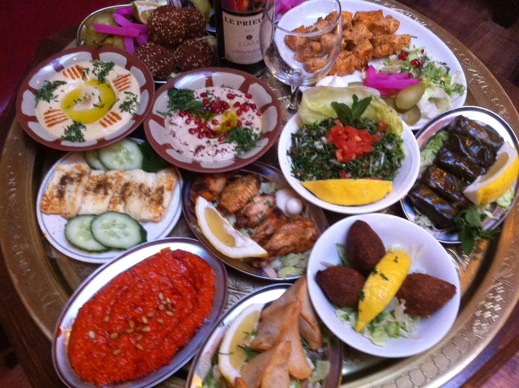 large lebanese platter of food including salads, aubergine wraps, chicken, lemon slices, shish kebabs, sweet desserts and some wine