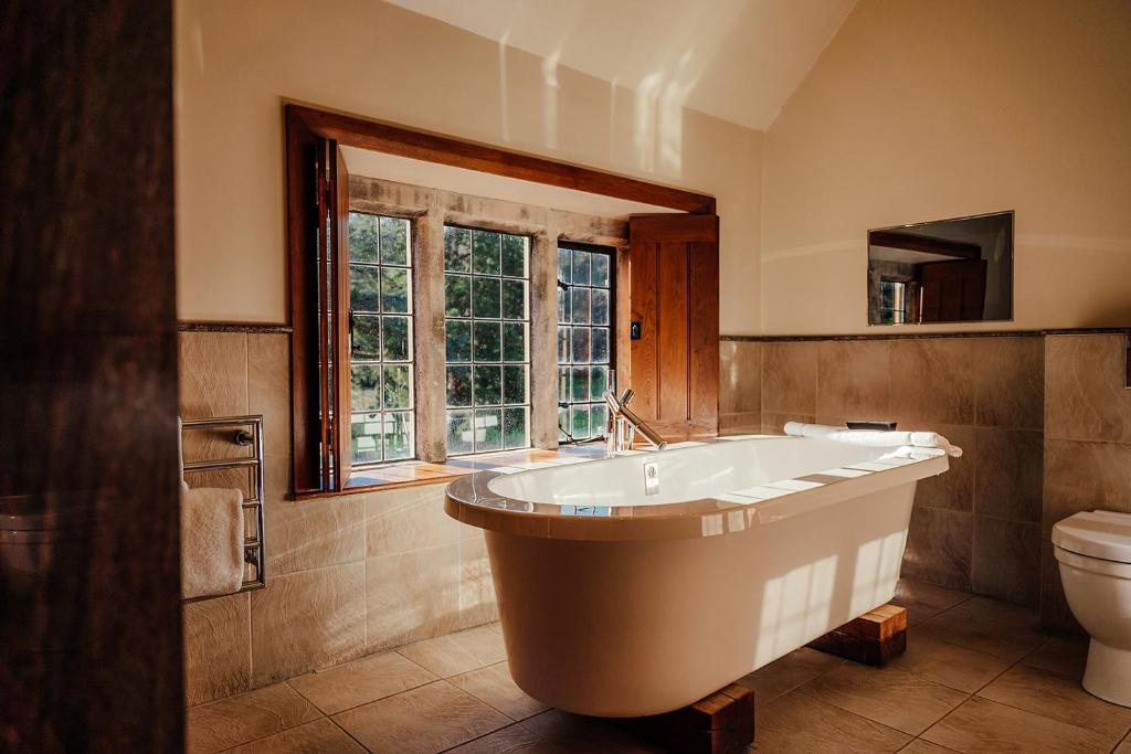 cream bathroom with a modern isolated white bathtub, panelled windows with wooden opener blinds, and white towels on a side table, at the Manor House in Castle Combe.
