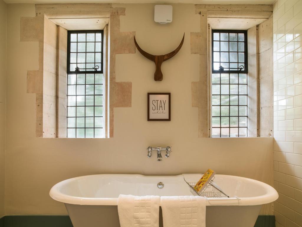 A luxurious bathroom at The Painswick hotel, featuring a freestanding bathtub, modern metro tiling, a wooden mounted horns decoration, tiled windows, and elegant brass fixtures.