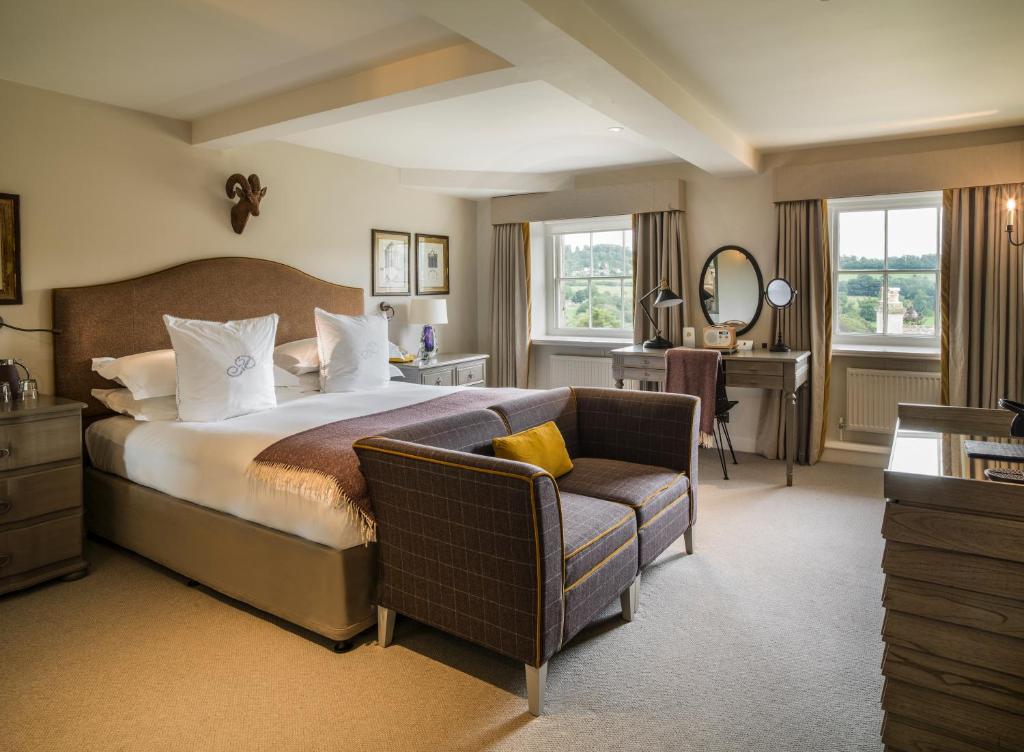 A spacious double bedroom at The Painswick, with a large upholstered headboard, vibrant contemporary art, and views over the Cotswold valley.