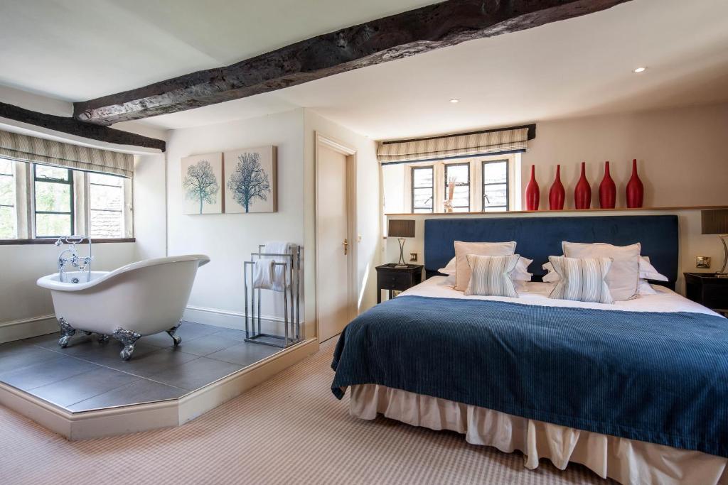 A luxurious, open-plan bedroom and bathroom suite featuring a freestanding bathtub placed beside the bed, at the slaughters inn.